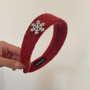 Détail d'un serre-tête en peluche rouge avec flocon en strass et étiquette faite main