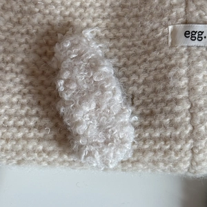 Beige knitted hair clip featuring plush rabbit ears and a minimalist egg label detail