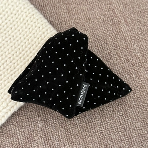 Detail view of black velvet hair clip with silver polka dots and fashion label on soft fabric