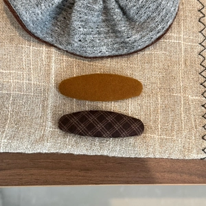 Detail view of brown plaid and velvet BB hair clips on textured fabric background