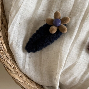 Detail of plush flower hair clip with black base, brown petals and purple bead center