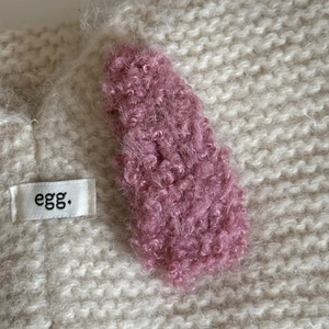 Close-up of pink faux shearling hair clip on a white knit sweater with soft texture