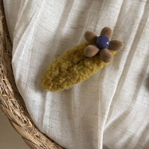 Detailed close-up of a plush ginger flower hair clip on a textured linen fabric background