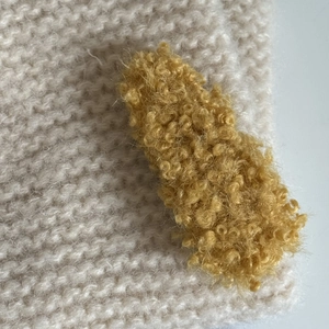 Close-up of fuzzy yellow lamb wool hair clip texture on beige knitted fabric background