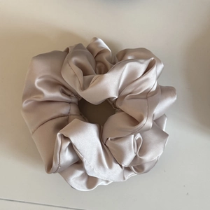 Detail of soft champagne gold satin scrunchie with pleated texture and glossy finish