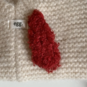 Close-up of deep red lamb wool hair clip on a white knit background showing soft texture