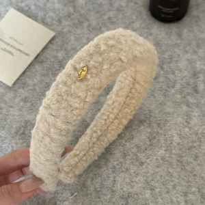 Detailed view of plush cream faux shearling headband with an oval gold logo accent