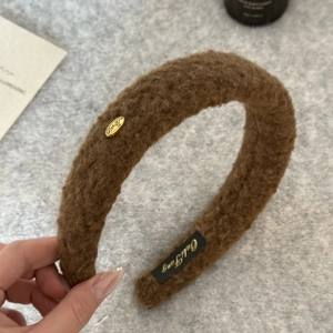 Detail of plush brown lamb wool headband featuring golden metal logo and brand tag