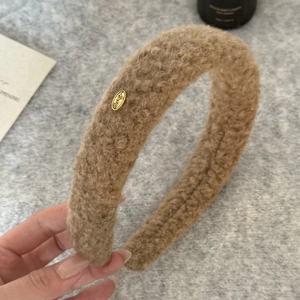 Detail shot of khaki teddy fur headband with oval gold metal label and soft plush texture