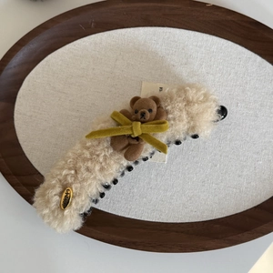 Dettaglio della clip per capelli in peluche con orsetto e fiocco su vassoio in legno