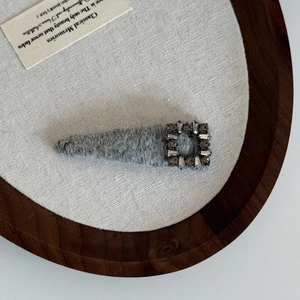 Detail view of grey wool texture and sparkling vintage rhinestone buckle on a hair clip