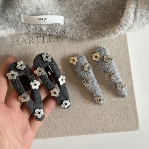 Close-up of gray wool knit hair clips with silver flower charms on a linen display board