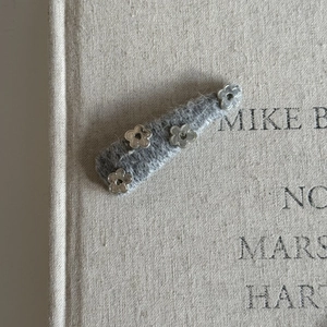 Gray wool hair clip with four silver metal floral accents on a minimalist vintage background