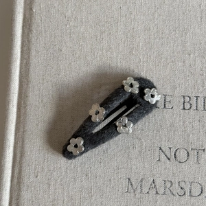 Detail of grey woolen hair clip with five silver flower charms on a textured fabric base