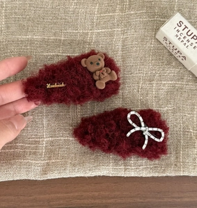 Detailed close-up of dark red plush hair clips with rhinestone bow and teddy bear charm