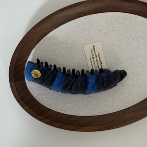 Plaid wool banana hair clip with gold logo detail on elegant wooden tray display