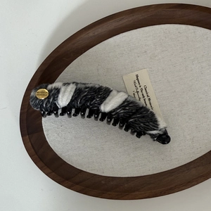Detail view of a striped wool banana hair clip featuring a vintage gold metal logo emblem