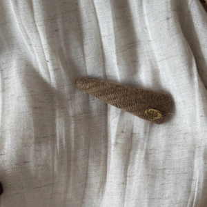 Detailed texture of a brown knitted hair clip with a gold 'Hand Made' metal badge label