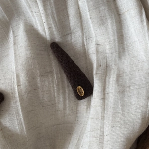 Detail view of a vintage coffee brown felt hair clip with a gold 'Hand Made' metal plaque