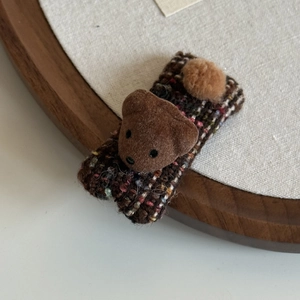 Detailed macro view of the brown plaid tweed fabric and flocked bear head on the hairpin