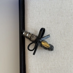 Close-up of rhinestone bow hair clip with gray felt and metal tag on linen board