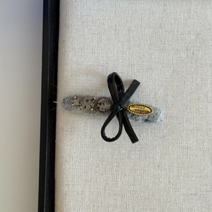 Detail view of a gray wool hair clip with rhinestones and a black leather bow decoration