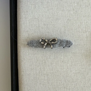 Dark grey plush hair clip with a luxury rhinestone bow design on a textured board