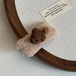 Close-up of a plush bear hair clip in brown and beige wool on a wooden tray