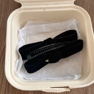 Detailed view of black velvet bow banana clip with fine glitter and gold oval metal tag