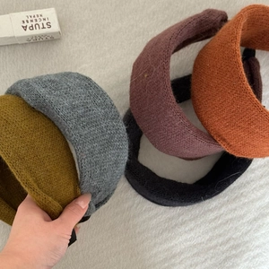 Hand holding assorted thick knit headbands in mustard yellow, orange and navy colors