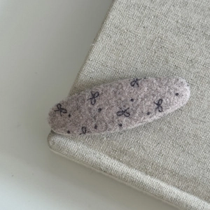 Pinkish brown woolen bow hair clip with black polka dots on a minimalist fabric base