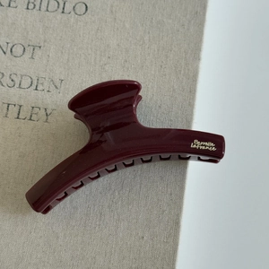 Pince à cheveux rouge foncé pailletée avec lettrage doré sur un fond en tissu élégant