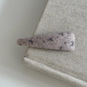 Close-up of lilac wool hair clip with black bow patterns on a fabric background