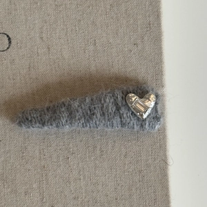 Detailed close-up of a grey plush hair clip with a silver heart-shaped rhinestone charm