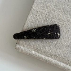 Detail of dark brown wool felt hair clip with white bow embroidery on linen texture