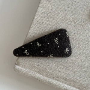 Close-up of a brown felt hair clip with cream bow embroidery on textured linen fabric