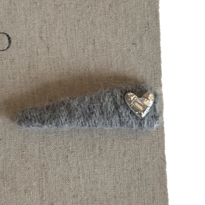 Plush grey hair clip with silver heart charm and crystal accent on soft fabric background
