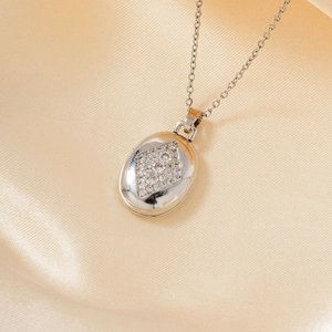 Collar con colgante ovalado de plata y centro de pavé de diamantes sobre fondo de seda champán
