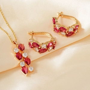 Makroaufnahme von Goldschmuck-Set mit roten Birnensteinen auf champagnerfarbener Seide