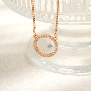 Close-up of rose gold circle necklace with pavé zirconia on a white plush surface