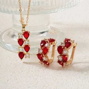 Detailaufnahme von Goldschmuckset mit roten und weißen Zirkonia-Steinen auf feinem Sand