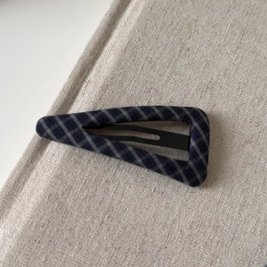 Detail of a navy blue plaid fabric triangular hair clip on a neutral linen background