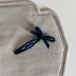 Détail de la pince à cheveux avec nœud en velours bleu marine sur fond de tissu en lin