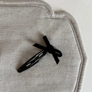 Détail d'un nœud en velours noir sur une barrette BB en métal sur fond de lin gris