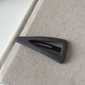Detail of a minimalist dark gray fabric-covered triangular hair clip on linen background