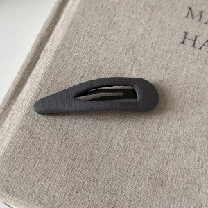 Close-up of charcoal grey twill fabric texture and metal inner clip of the BB hair pin