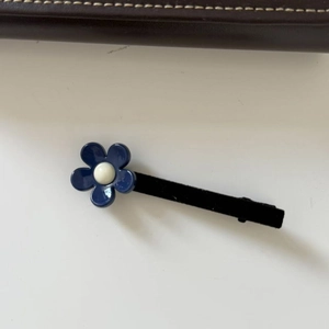 Détail d'une pince à cheveux fleur bleue avec perle centrale sur un support en tissu noir