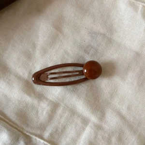 Close-up of caramel brown teardrop hair clip with glossy metallic finish on fabric