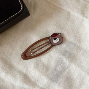 Cute brown bear hair clip with red beret on white linen fabric from a stylish side angle