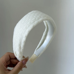 Handheld view of a wide white lace headband featuring elegant vintage floral patterns